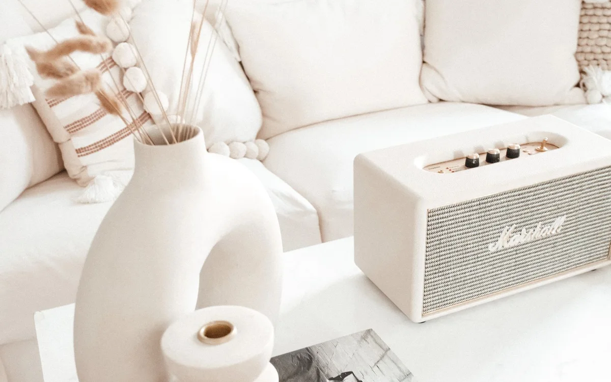 A cream-colored speaker sits beside vases on a living room coffee table.
