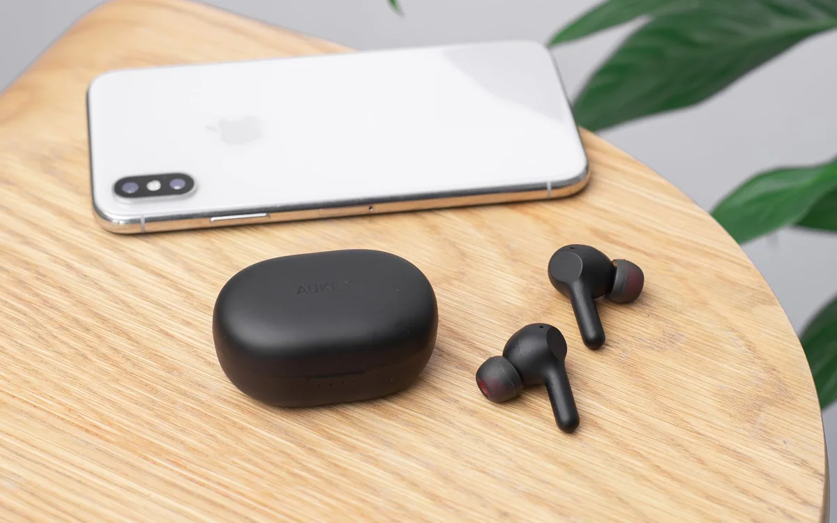 Wireless earphones and a smartphone on a wooden table indoors.