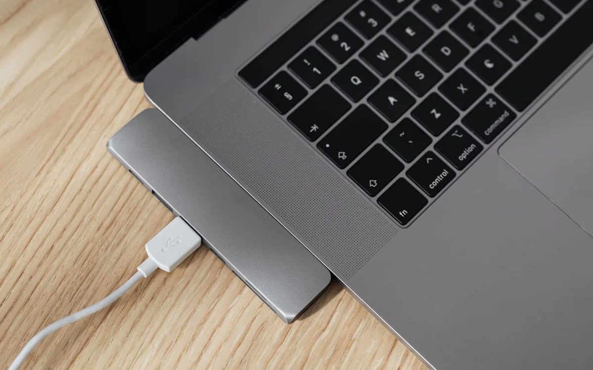 A laptop is connected to a USB-C hub and white cable on a wooden desk.
