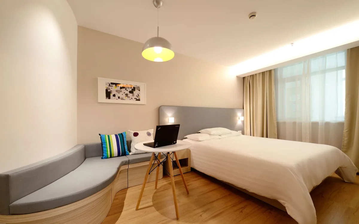 A laptop rests on a desk in a furnished hotel room.