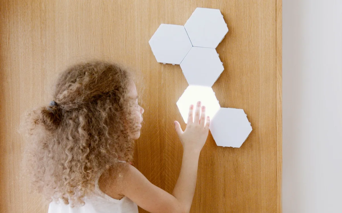 A girl touches illuminated hexagonal light panels on a wall.