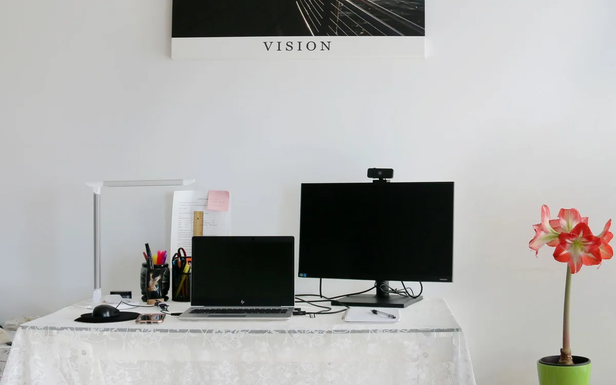 A laptop and monitor with a webcam share a white home office desk.